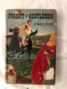 Book jacket of Pursuit of Gentlemen, in which a busty blonde in a low cut long red dress loosely aims a rifle at a gentleman riding a badly controlled horse. The general style is that of the poster for a comic Western